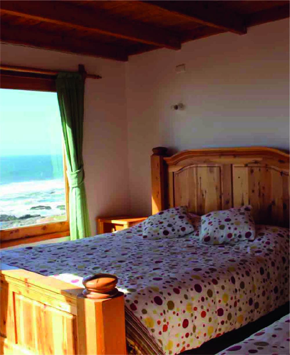 Habitación de la hostería con cama de madera y ventanal al mar